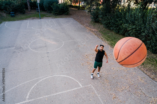 basketball player shoots the ball from a distance on a quiet outdoor court surrounded by greenery, emphasizing focus and skill under soft evening light with scattered leaves on the ground.