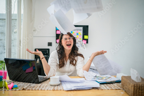 A stressed woman in a cluttered home office is throwing papers into chaos all around her