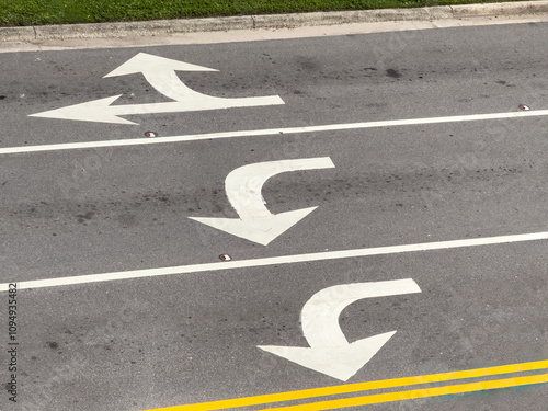 High-angle view of white directional arrows in three turn lanes near an intersection (off camera) of an urban one-way street downtown, for themes of alternatives, guidance, and impending decisions