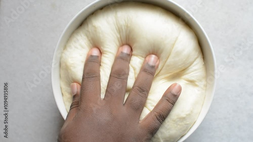 Overhead view of proofed challah dough being deflated, top view of hand deflating dough in a white mixing bowl, process of making challah