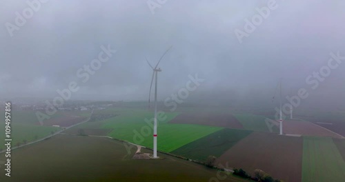 Aerial video showcasing wind turbines on farmland, partially hidden by low-hanging clouds on a misty day