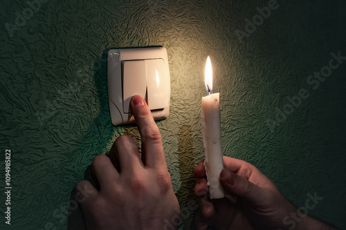 Holding burning candle in a dark room near a light switch, blackout. Power outage, energy crisis. Problems with power supply. Ukraine without power