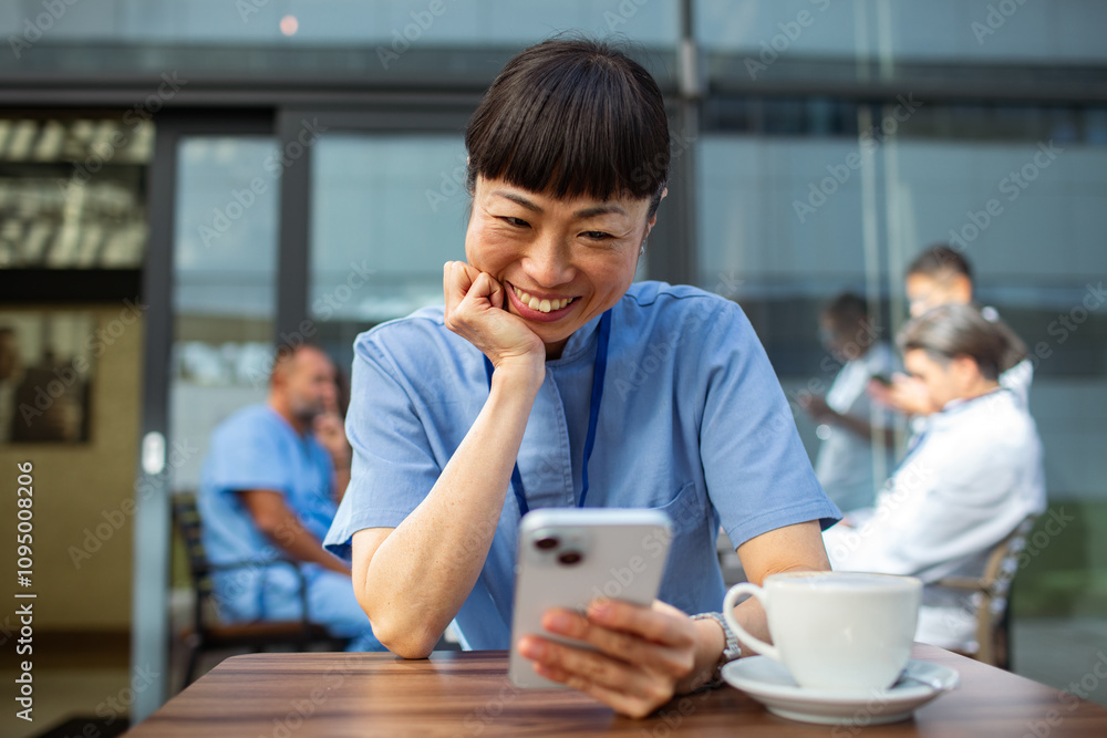 Smiling Asian nurse using smartphone on coffee break Smiling Asian nurse using smartphone on coffee break