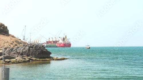 A red ship is docked at a pier next to a rocky shore
