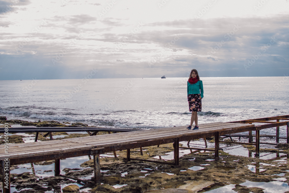 a young woman in bright clothes on an old rusty pier on the seashore, Ayia Napa, Cyprus a young woman in bright clothes on an old rusty pier on the seashore, Ayia Napa, Cyprus