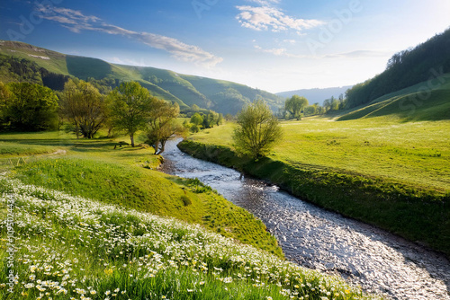 A serene river flows through a springtime valley, lush with green grass and wildflowers, nestled between towering mountains, ai.