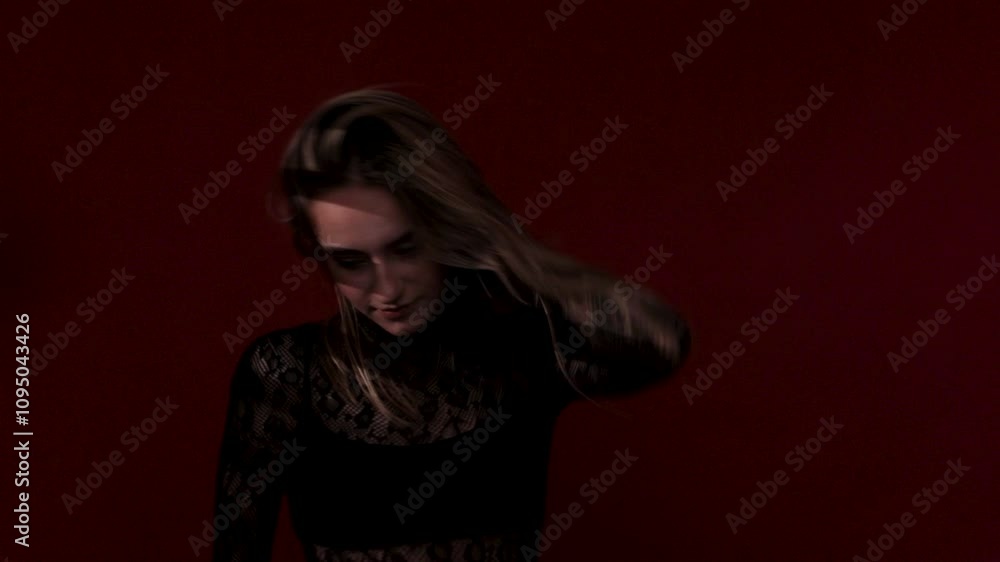 Slender sexy woman in a mesh jumpsuit dances on a dark red background. Her body is illuminated by red lights. Slender sexy woman in a mesh jumpsuit dances on a dark red background. Her body is illuminated by red lights.