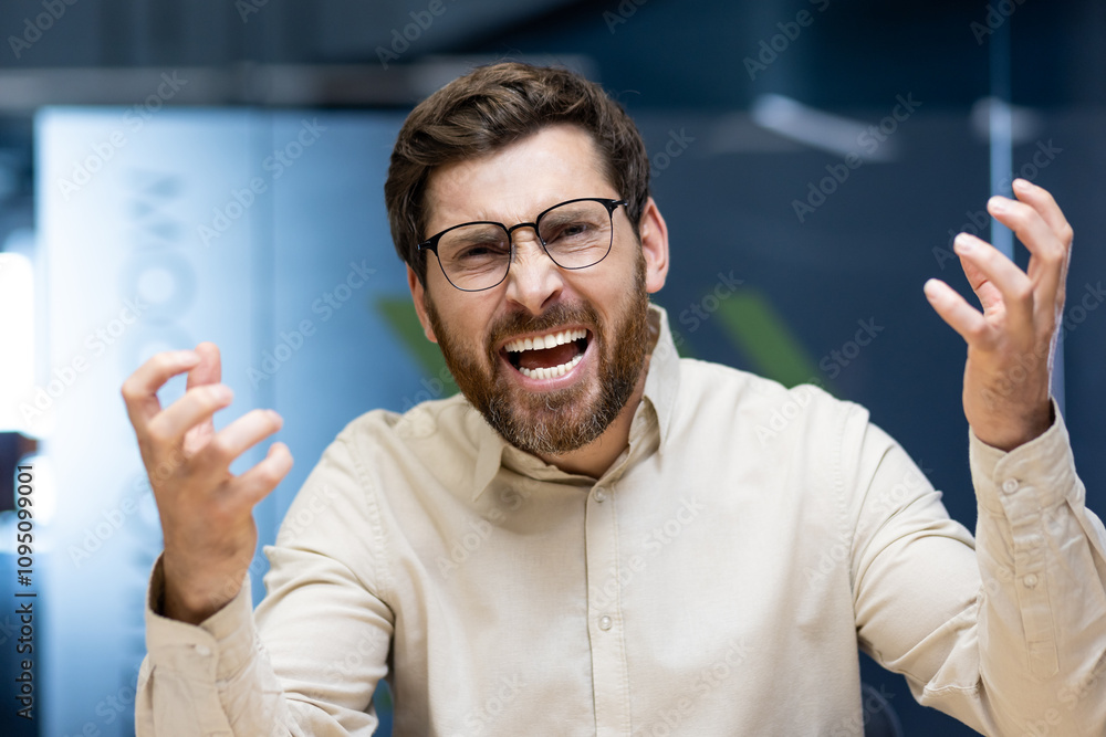 Close-up portrait of a young man in glasses and a shirt who is in the office and angrily talking and shouting at the camera while gesturing with his hands Close-up portrait of a young man in glasses and a shirt who is in the office and angrily talking and shouting at the camera while gesturing with his hands