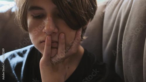 Wallpaper Mural Teenager sitting on a couch, touching his face slowly, reflecting feelings of worry and contemplation in a casual indoor setting Torontodigital.ca