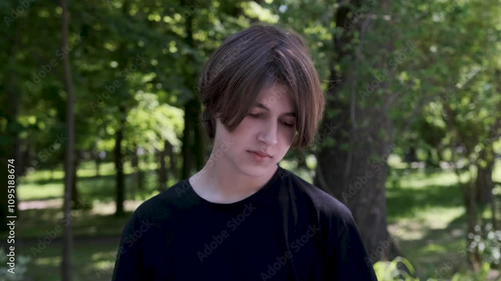 Young adult male is running his fingers through his hair while experiencing sadness in a tranquil park setting, captured in slow motion Young adult male is running his fingers through his hair while experiencing sadness in a tranquil park setting, captured in slow motion