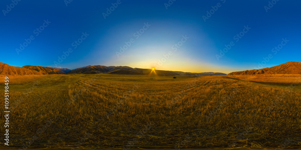 Fototapeta premium Full Spherical panorama of straw moved agricultural field surrounded with foothills at autumn sunset with blue sky in equirectangular projection