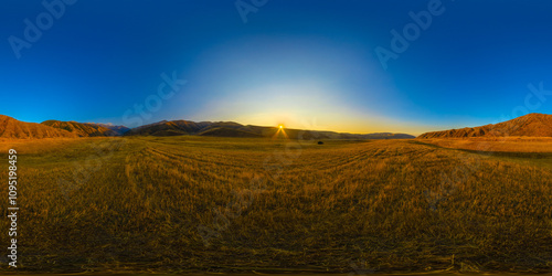 Full Spherical panorama of straw moved agricultural field surrounded with foothills at autumn sunset with blue sky in equirectangular projection