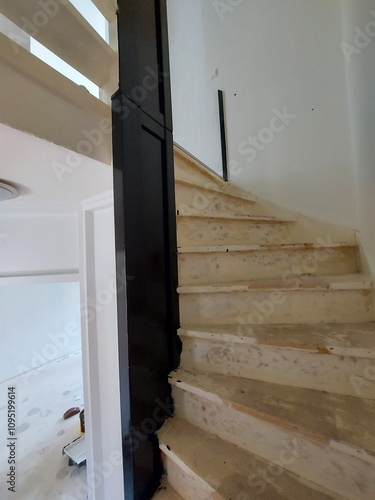 A modern staircase with wooden steps and a sleek black railing. The staircase leads up to a loft or second floor. The image showcases the clean lines and minimalist design of the staircase.