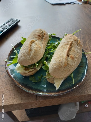 A pair of delicious-looking sandwiches on a plate. Each sandwich is filled with brie cheese and fresh rocket leaves, served on a crusty roll