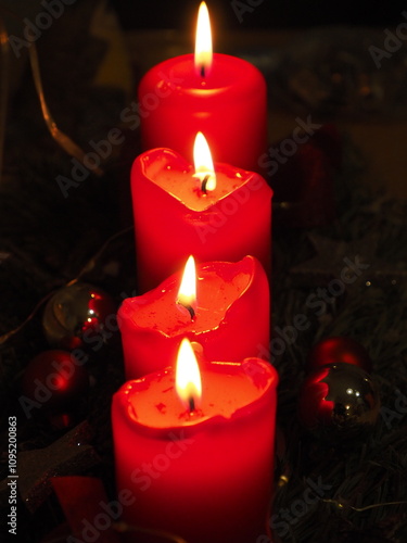 Weihnachtliche Stimmung mit vier roten Kerzen, die hintereinander auf einem Adventsgesteck stehen, ihr Licht leuchtet in der Dunkelheit,  photo