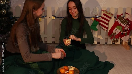 Family decorating christmas tree together. Subdued cinematic light. Cheerful girlfriends. Two girls eating tangerines near a Christmas tree. Friendship. Fun and laughter. 