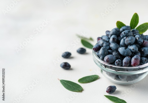 Ripe honeysuckle berries overflowing a glass bowl, accompanied by vibrant green leaves, creating a fresh and healthy image