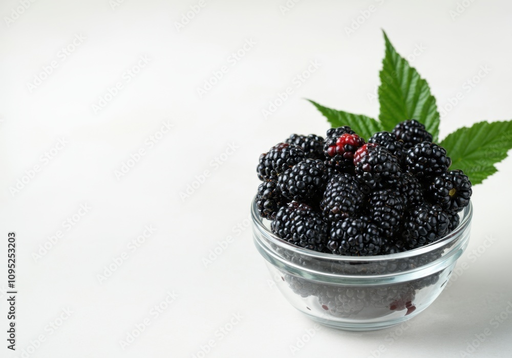 Ripe blackberries with green leaves are served in a glass bowl, creating a healthy and delicious presentation Ripe blackberries with green leaves are served in a glass bowl, creating a healthy and delicious presentation