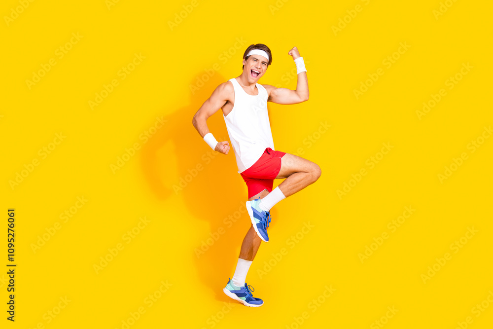 Energetic young man in sportswear expressing happiness against vibrant yellow background Energetic young man in sportswear expressing happiness against vibrant yellow background