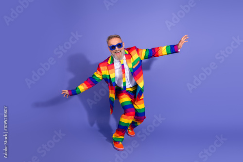 Vibrant senior man in rainbow suit enjoys disco vibes on a stunning violet backdrop