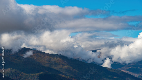 the tops of the mountains surrounded by thick swirling clouds against the blue sky