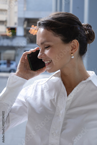 Businesswoman is talking on the phone, smiling. Close-up, place for text. Wearing a white shirt and has a bun hairstyle. Promo, logo, advertising. Business concept photo