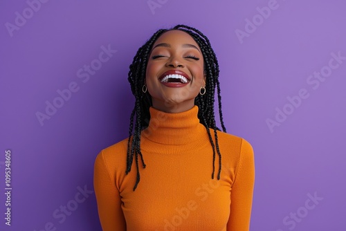 Joyful woman in orange sweater with braided hair against purple wall photo