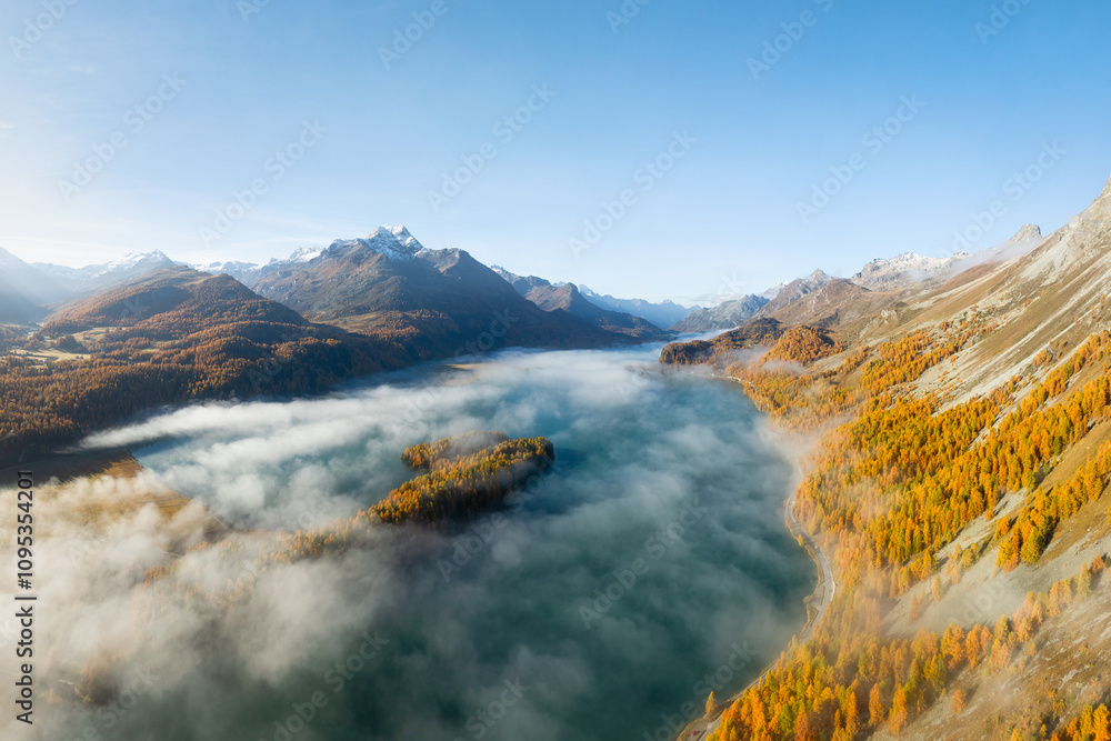 Obraz premium Drone view of a mountain valley with fog. Engadin valley, Switzerland. Autumn landscape from the air. Sun rays in the mountains. Photo for background, wallpaper, postcards.