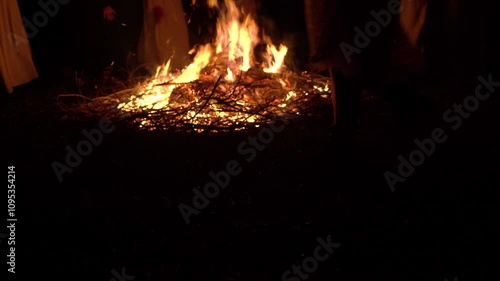 Unrecognizable people dance circle around a big campfire at night. View people legs 4K