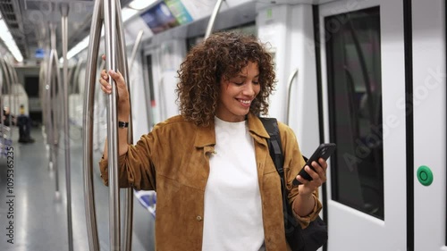 Wallpaper Mural Young woman stands on a subway train, holding a smartphone and browsing social media with a smile.  Woman browsing social media on subway in slow motion Torontodigital.ca