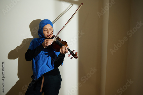 Woman wearing a blue hijab playing the violin indoors photo