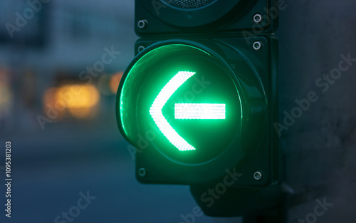 Close-up of a green traffic light with an arrow pointing left, indicating a signal to proceed.