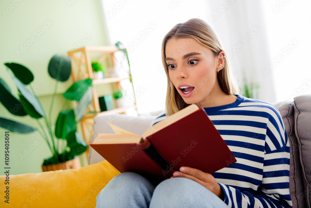 Photo of nice blonde young girl sit couch amazed read book wear striped clothes enjoy modern cozy interior flat indoors