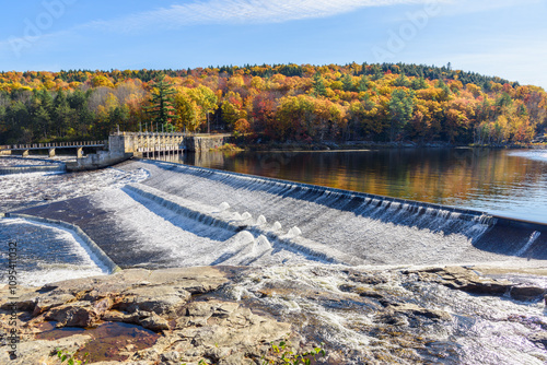 Hydroelectric dam along a river with forested banks at the peak of autumn colours on a sunny day photo