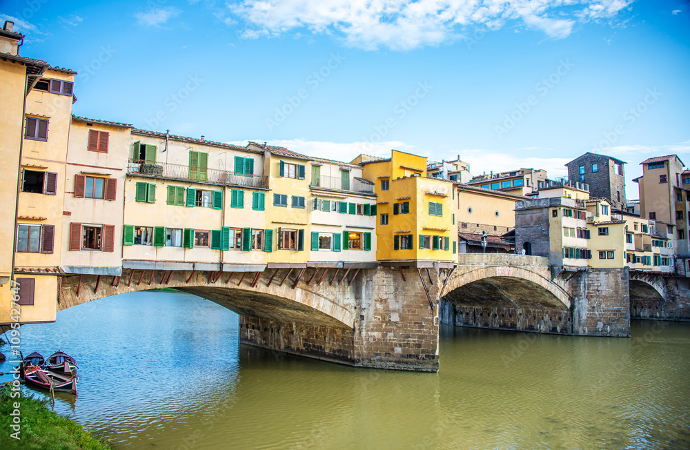 The Ponte Vecchio, the stone, pedestrian bridges in Tuscany, stands on its arched columns with its various retail shops open for business, shining in the sun above the Arno River in Florence, Italy. The Ponte Vecchio, the stone, pedestrian bridges in Tuscany, stands on its arched columns with its various retail shops open for business, shining in the sun above the Arno River in Florence, Italy.