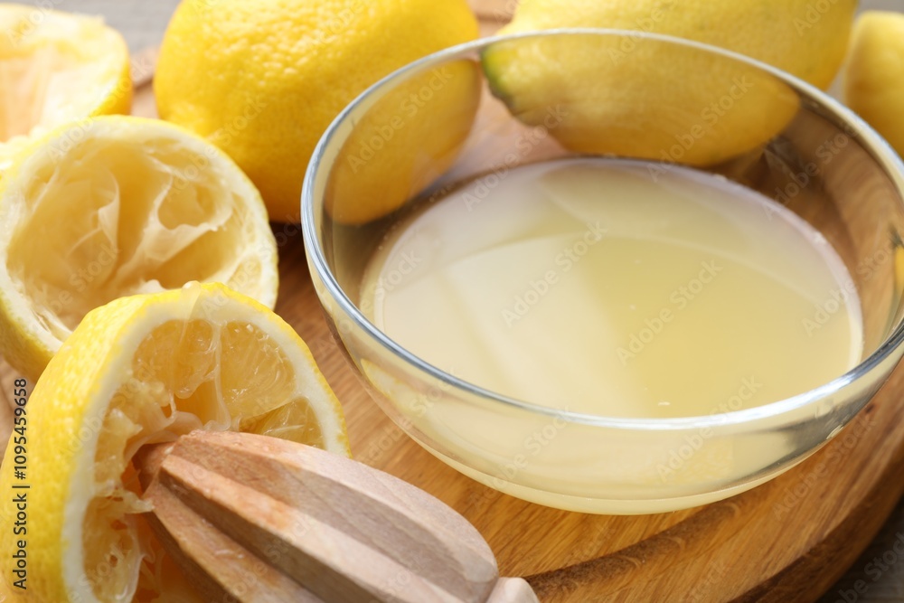 Bowl with fresh lemon juice, squeezer and fruits on wooden table, closeup Bowl with fresh lemon juice, squeezer and fruits on wooden table, closeup