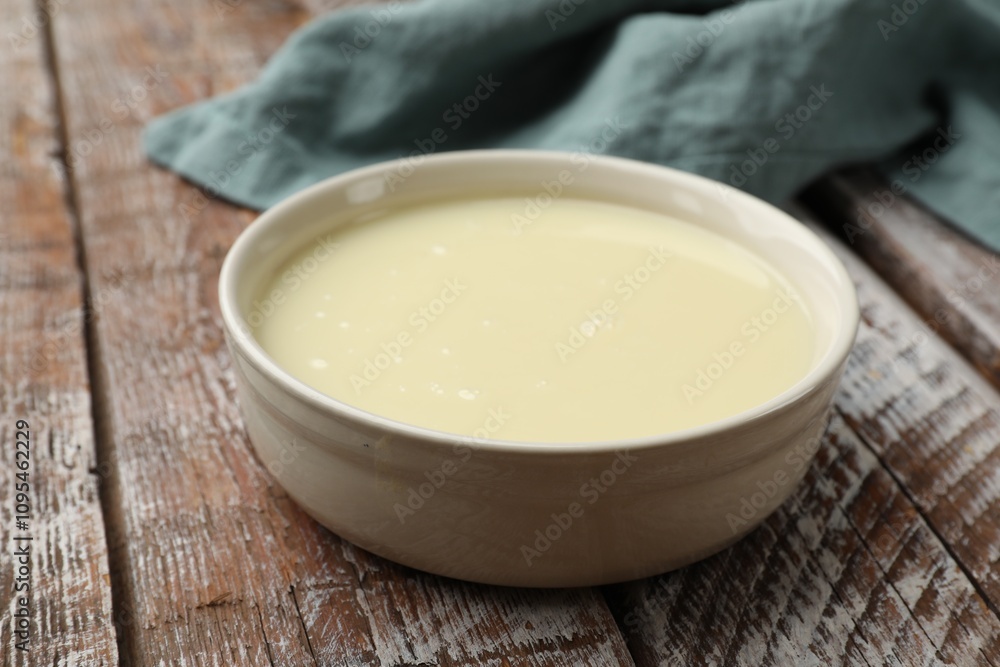 Condensed milk in bowl on wooden table, closeup Condensed milk in bowl on wooden table, closeup