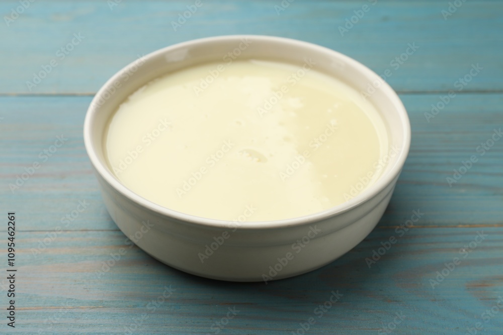 Condensed milk in bowl on light blue wooden table, closeup Condensed milk in bowl on light blue wooden table, closeup