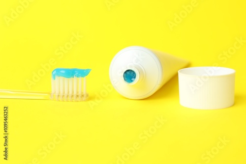 Toothbrush with toothpaste and tube on yellow background, closeup