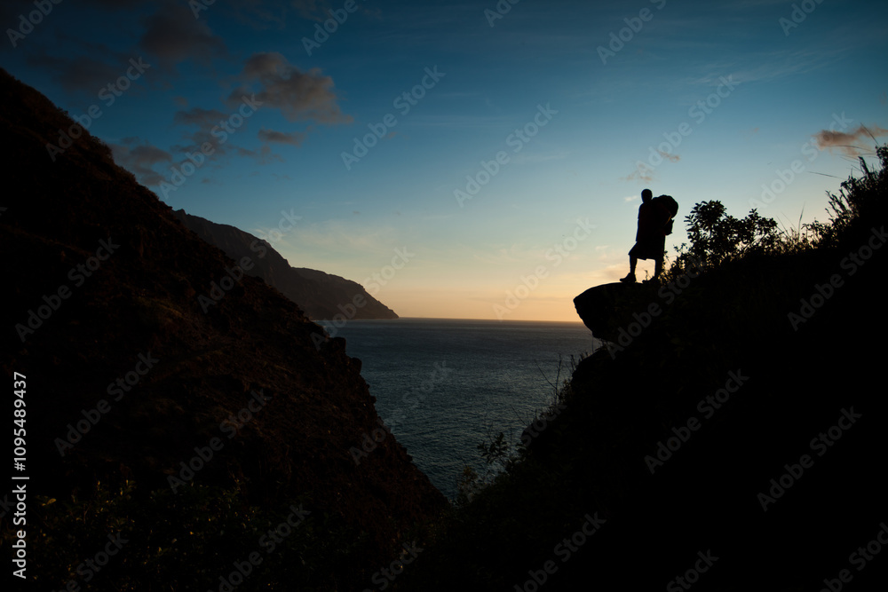 Silhouette of backpacker on island cliffside at dusk Silhouette of backpacker on island cliffside at dusk
