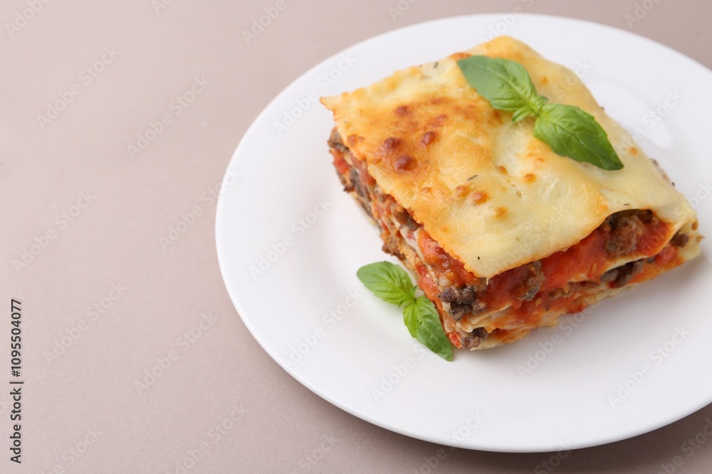Piece of delicious cooked lasagna with basil on beige background, closeup. Space for text Piece of delicious cooked lasagna with basil on beige background, closeup. Space for text
