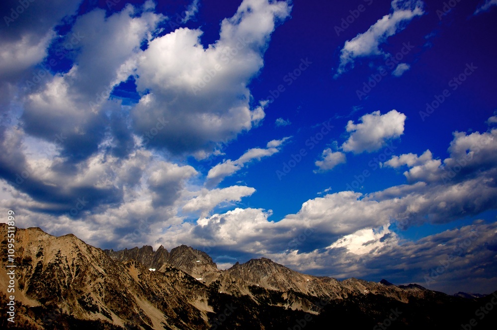 Beautiful, white, puffy clouds scattered across sky over rocky mountains - wide shot Beautiful, white, puffy clouds scattered across sky over rocky mountains - wide shot