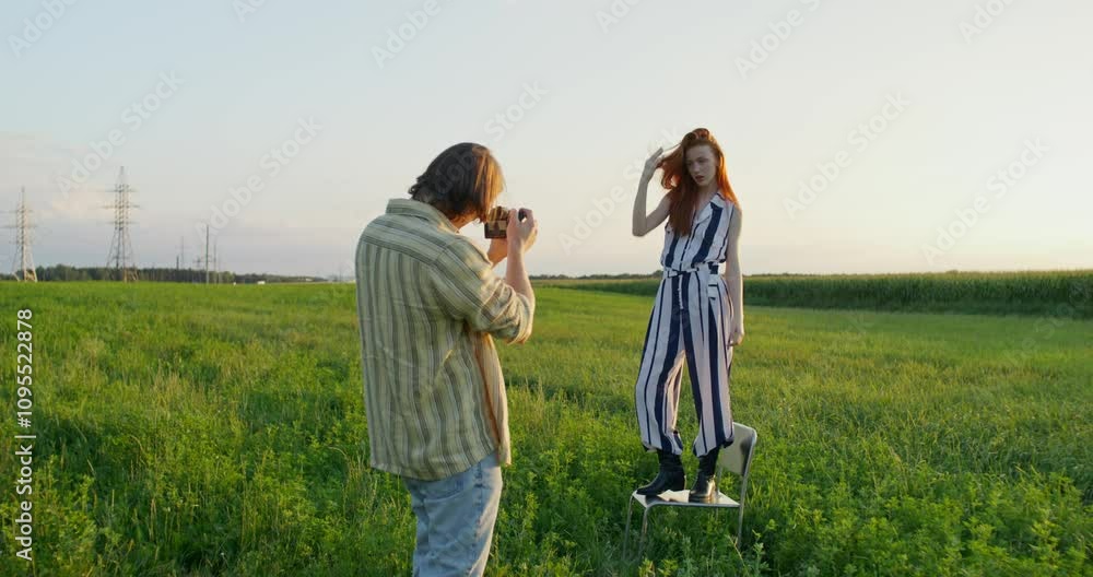 A man takes pictures of a young woman at sunset in a field. A woman poses standing on a chair A man takes pictures of a young woman at sunset in a field. A woman poses standing on a chair