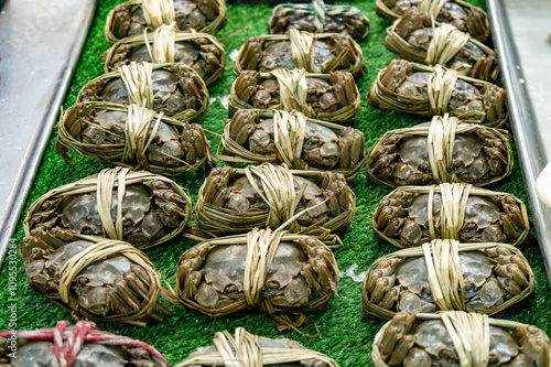 Many hairy crabs(Raw shanghai hairy crabs) wrapped in bamboo shoots, displayed on a green carpet at a market counter. photo