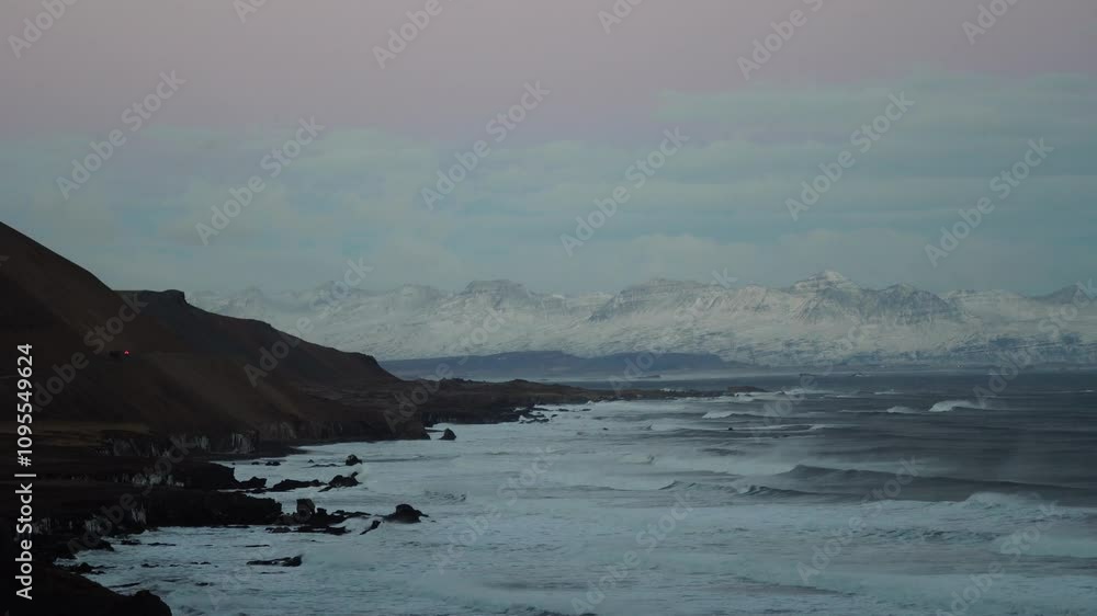 Red car drives along a stunning coastline, heading toward majestic snowy mountains in a picturesque winter landscape Red car drives along a stunning coastline, heading toward majestic snowy mountains in a picturesque winter landscape