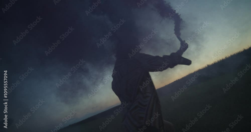 A young woman blows pink and blue smoke running across a field on a summer evening A young woman blows pink and blue smoke running across a field on a summer evening