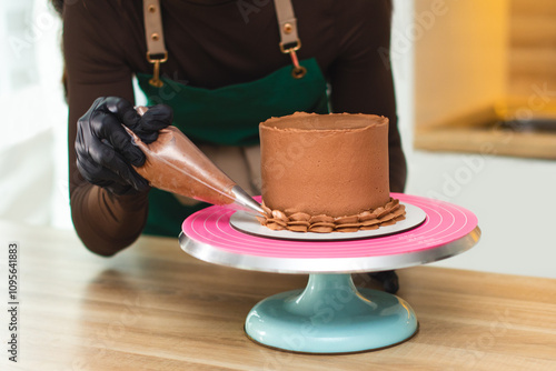 The process of a confectioner applying chocolate cream from a pastry bag onto a cake.