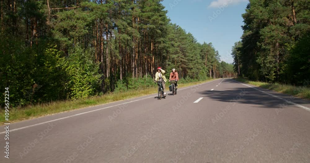 A young couple is riding a bike on a road in the middle of the forest. Active leisure on a sunny day A young couple is riding a bike on a road in the middle of the forest. Active leisure on a sunny day