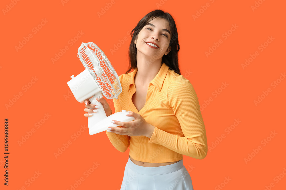 Young woman with electric fan on orange background Young woman with electric fan on orange background