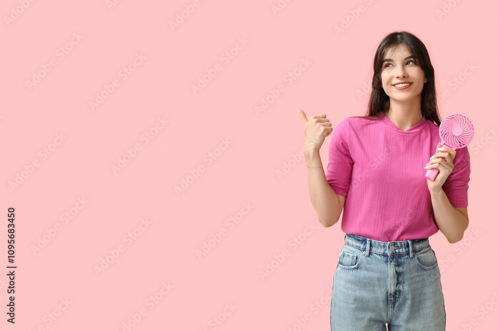 Young woman with mini fan pointing at something on pink background Young woman with mini fan pointing at something on pink background
